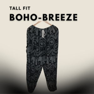 Tall fit black harem pants with elephant and mandala patterns, displayed hanging on a wooden hanger against a light beige gradient background.